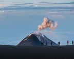 Volcano erupting with people observing from a distance against a blue sky in Mount Fuego, Guatemala.