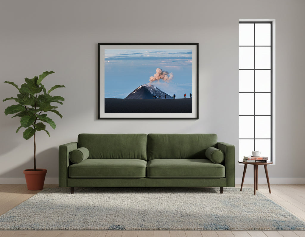 Framed volcano erupting with people observing from a distance against a blue sky in Mount Fuego, Guatemala.