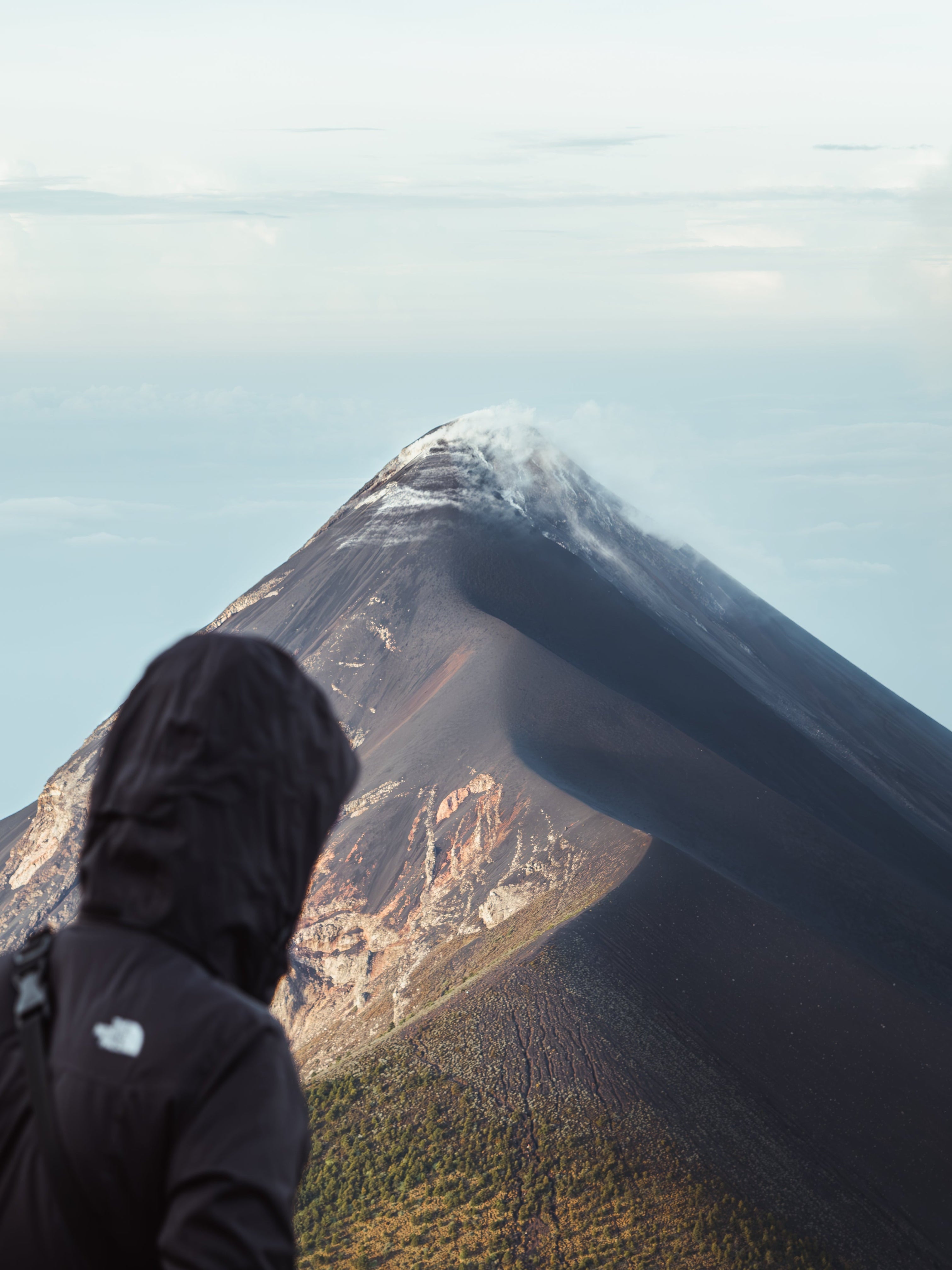Person in a black jacket standing on a mountain with a large mountain peak in the background