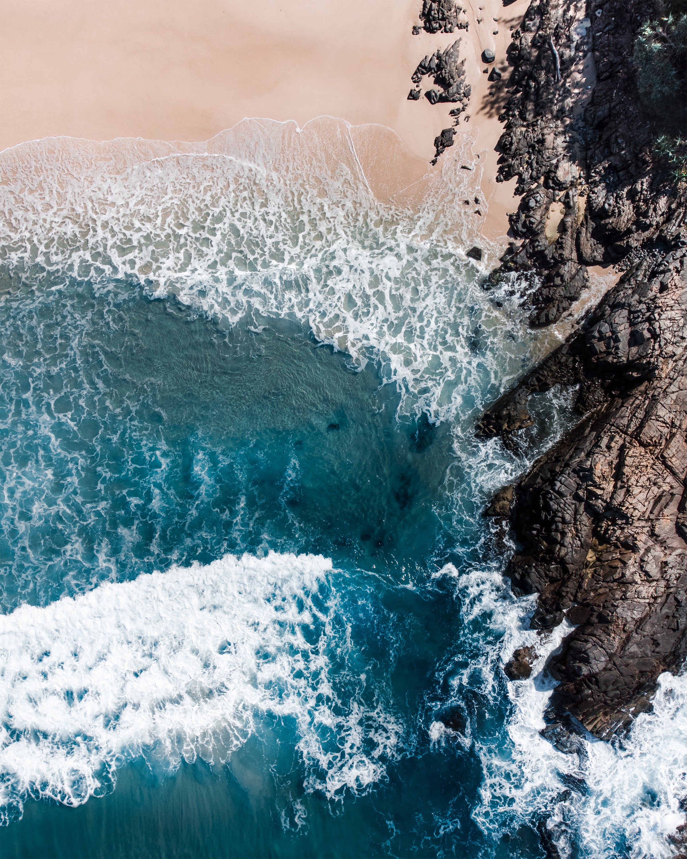Top-down view of blue waves crashing against a rocky shore in Noosa, Queensland, Australia.