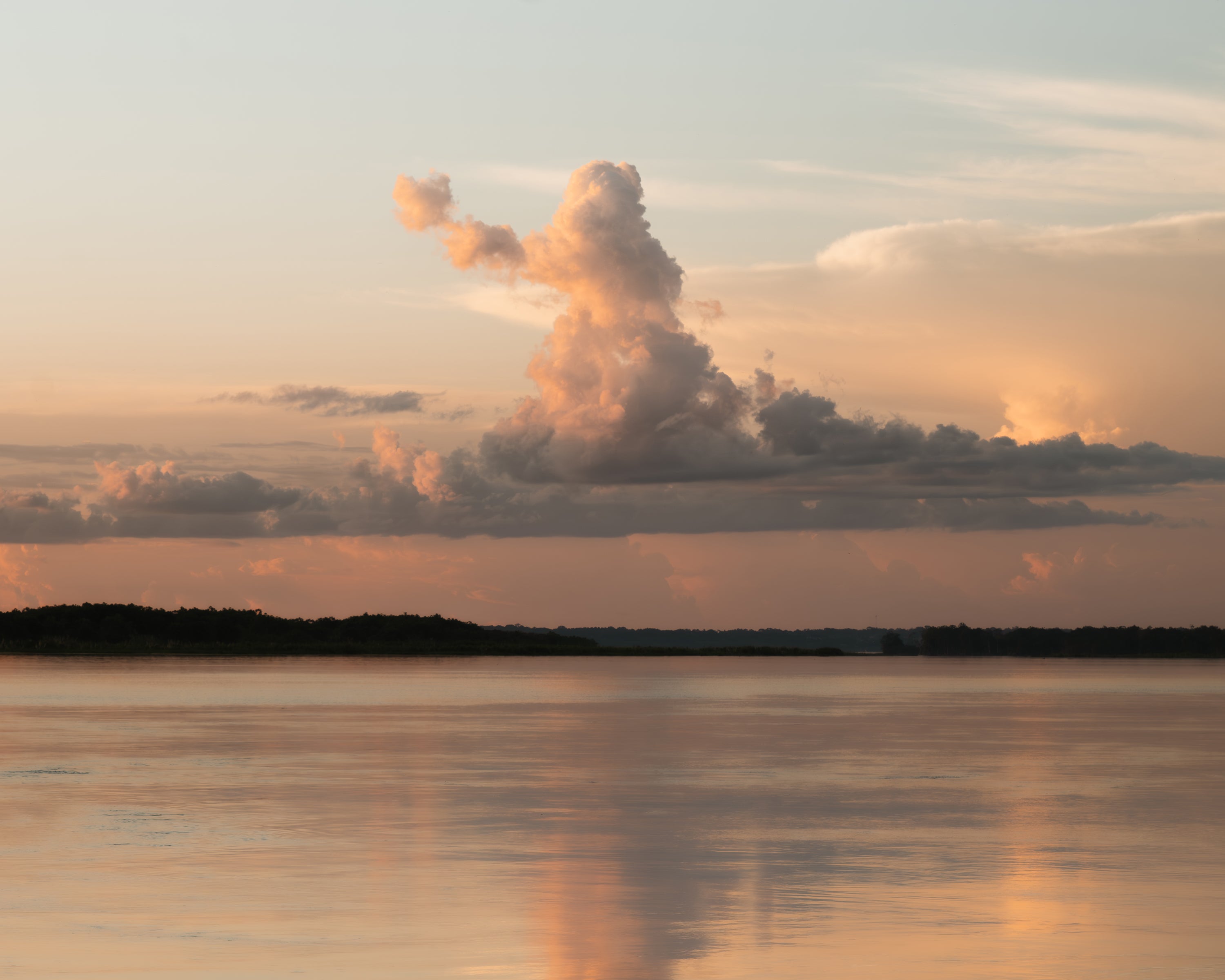 Beautiful, orange and peach sunset over a calm body of water with large clouds in the sky in the Amazon in Peru.