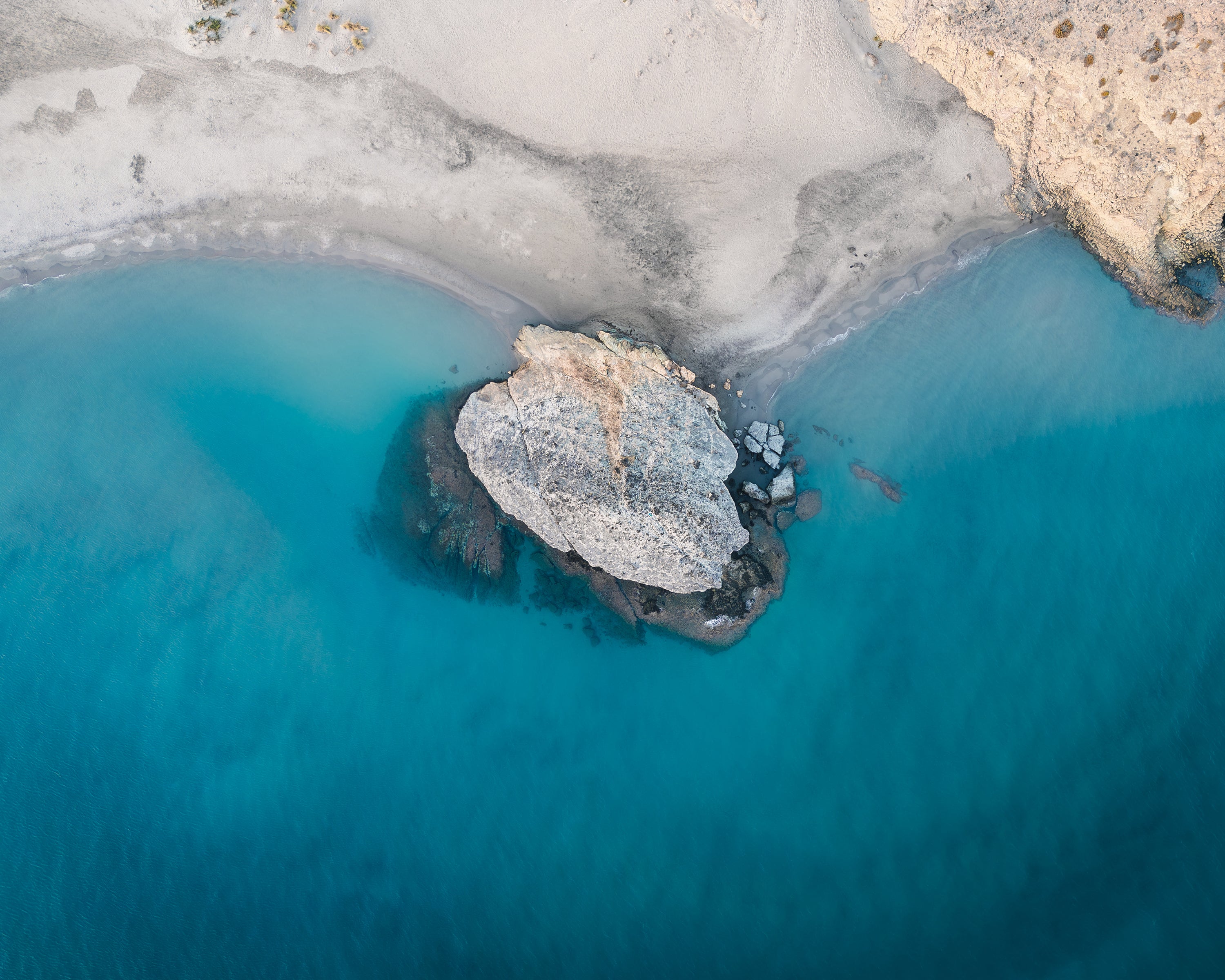 Aerial view of a rocky island in clear blue water with a white sandy beach in Cabo de Gata, Spain.