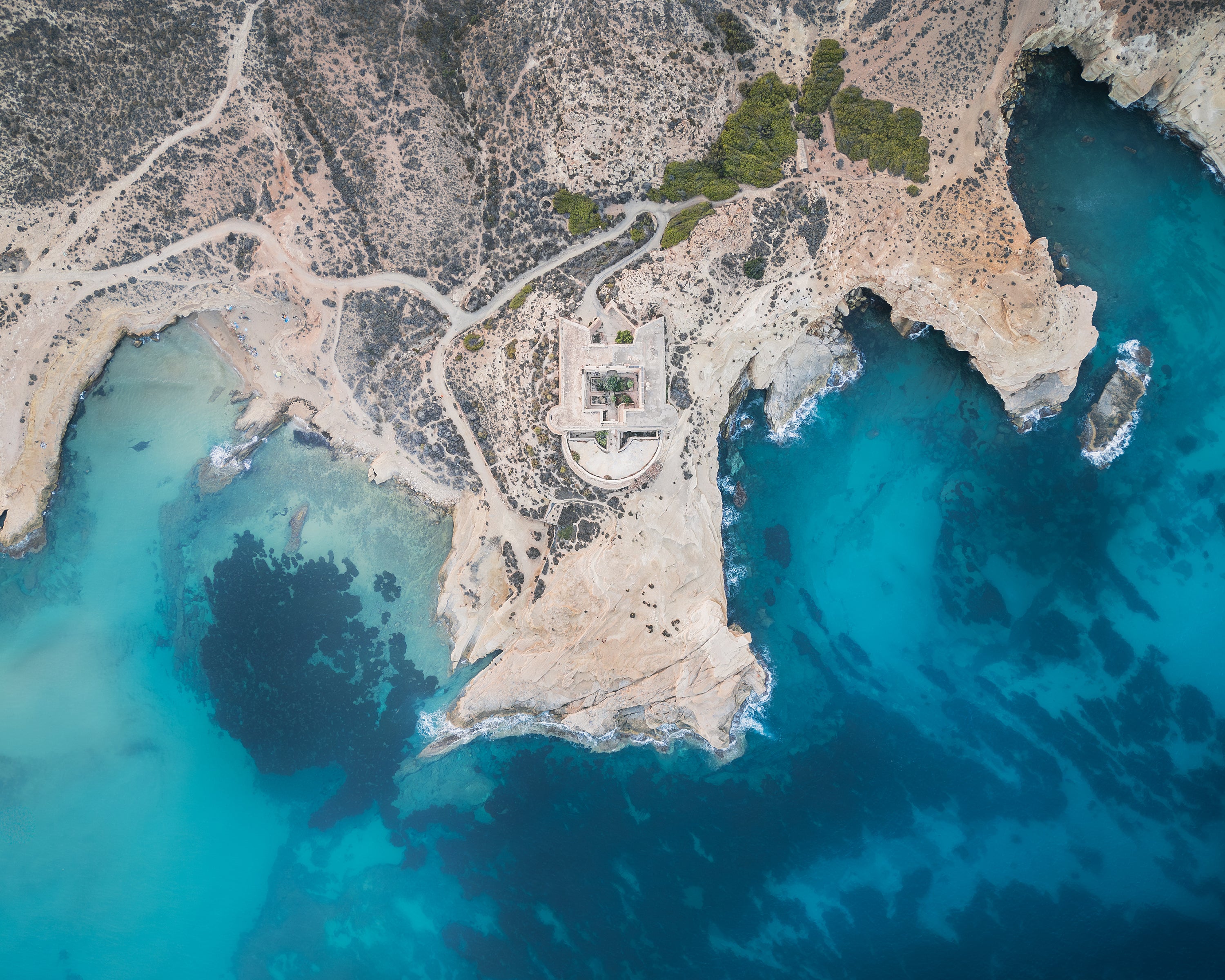 Aerial view of a coastal landscape with a castle surrounded by turquoise waters, in Cabo de Gata, Spain.