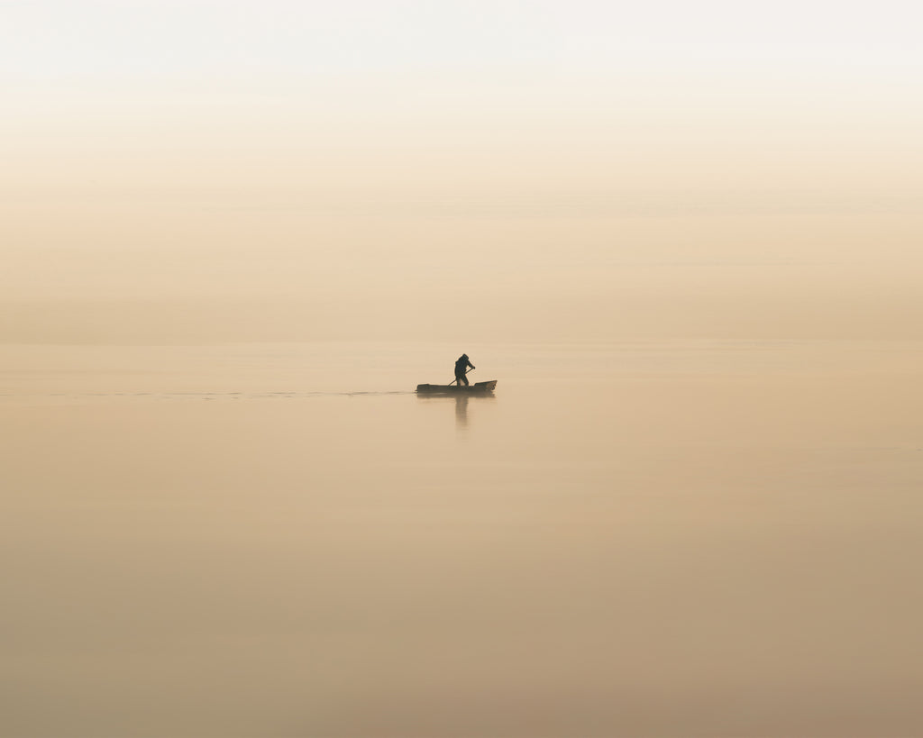 Lone fisherman at dawn rowing across a foggy, orange lake in Lake Atitlan, Guatemala.