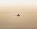 Lone fisherman at dawn rowing across a foggy, orange lake in Lake Atitlan, Guatemala.