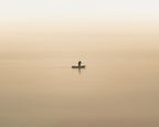 Lone fisherman at dawn rowing across a foggy, orange lake in Lake Atitlan, Guatemala.