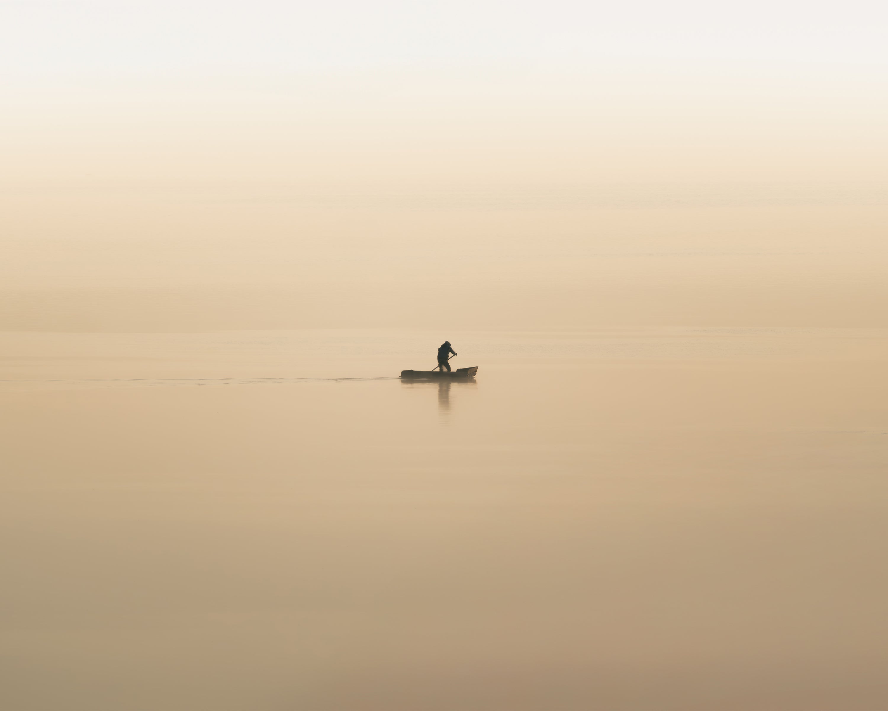 Lone fisherman at dawn rowing across a foggy, orange lake in Lake Atitlan, Guatemala.