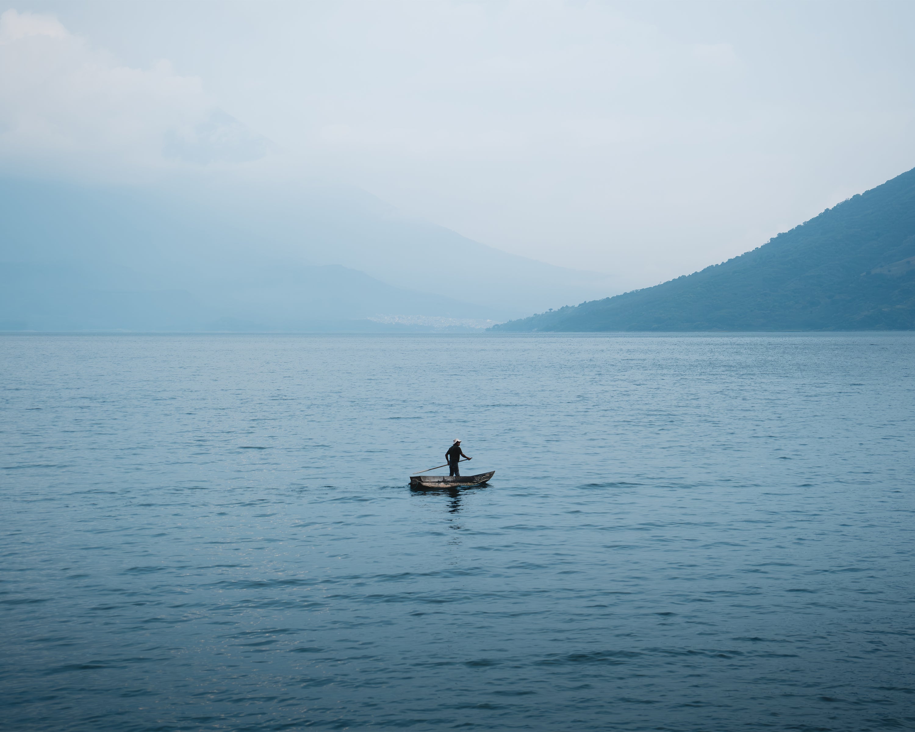 Person on a small fishing boat on a calm lake with mountains in the background, in Lake Atitlan, Guatemala.