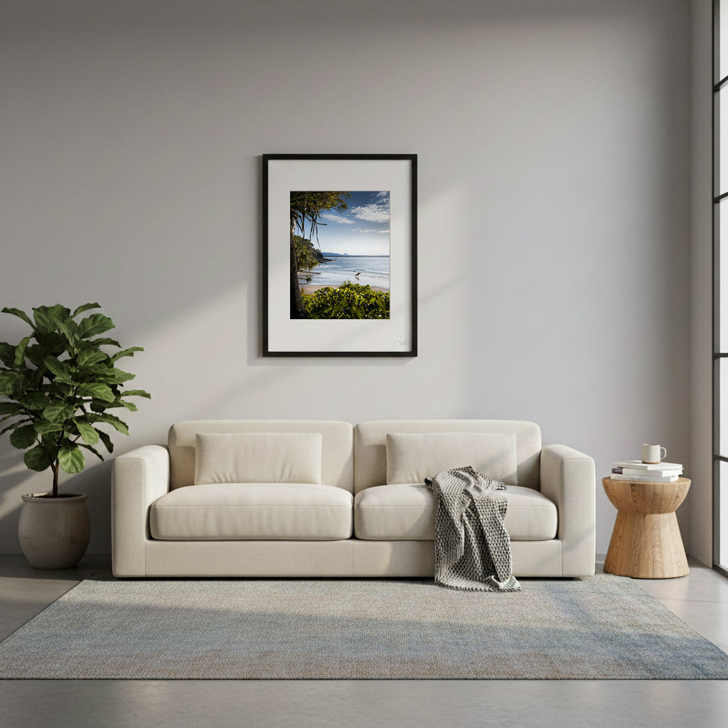 Framed beach scene with a person holding a surfboard, surrounded by greenery and clear sky in Noosa, Queensland, Australia. 