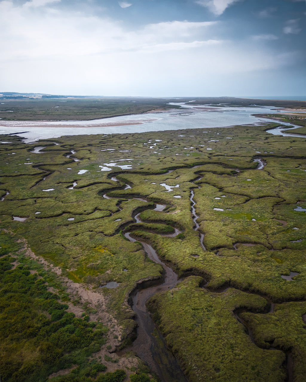 Wetland landscape with winding rivers and marshes under a blue sky in Norfolk, UK.