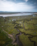 Wetland landscape with winding rivers and marshes under a blue sky in Norfolk, UK.