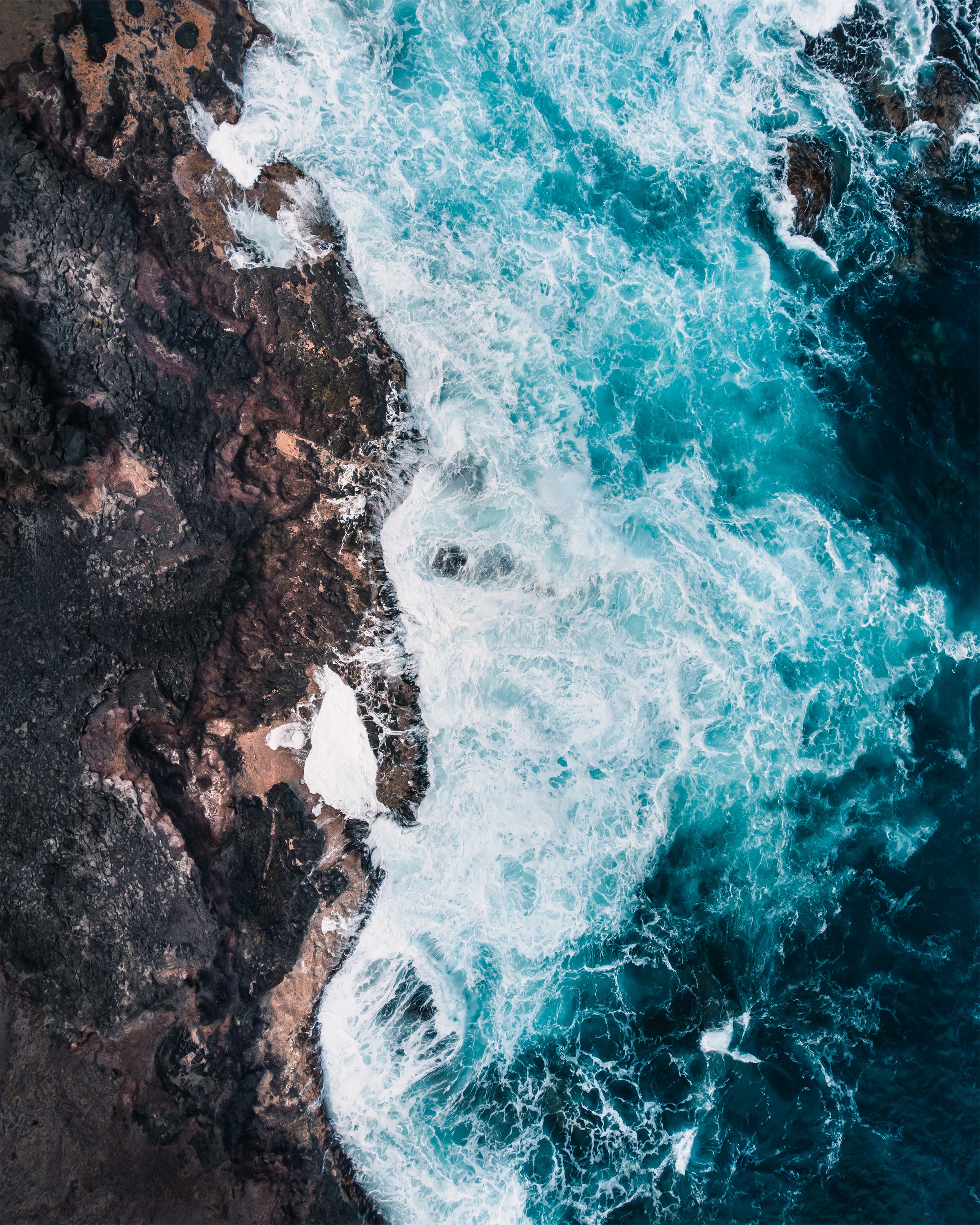 Turquoise ocean waves crashing against dark rocks in Cape Schank, Victoria, Australia.
