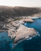 Rocky coastline with a fort-like structure surrounded by clear blue water, in Cabo de Gata, Spain.