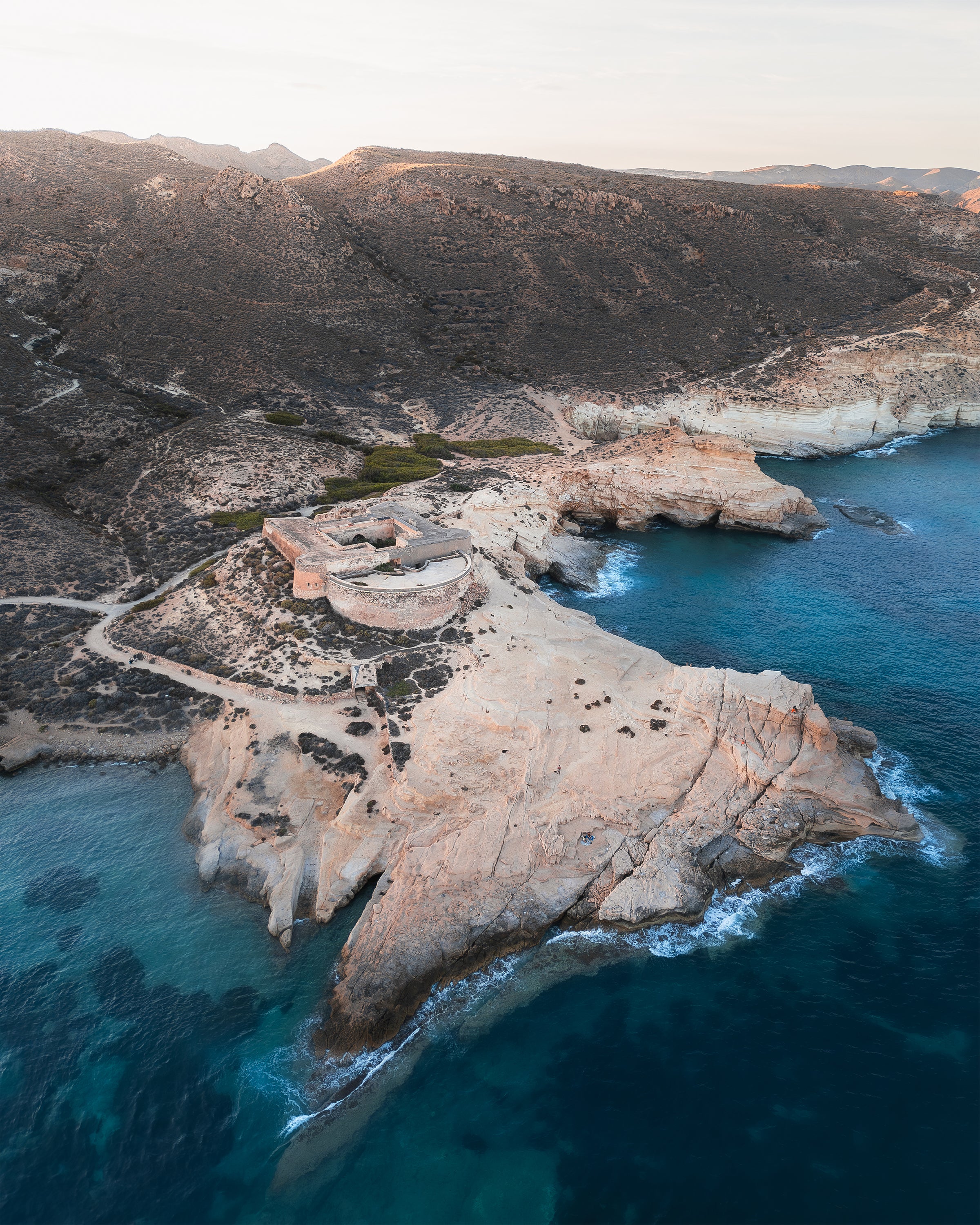 Rocky coastline with a fort-like structure surrounded by clear blue water, in Cabo de Gata, Spain.