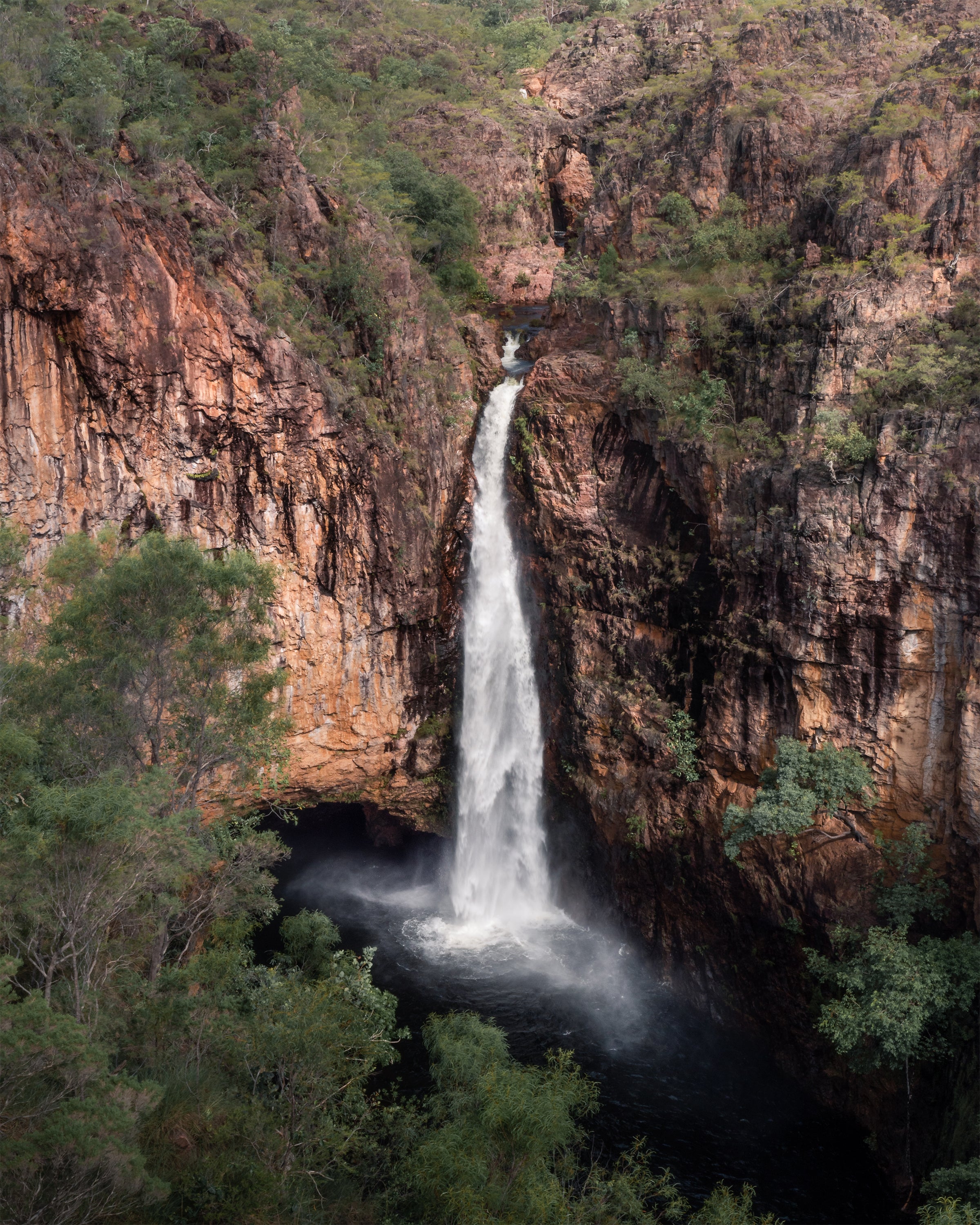 Waterfall cascading down a rocky cliff face with greenery around in Tolmer Falls, Litchfield National Park, Northern Australia.